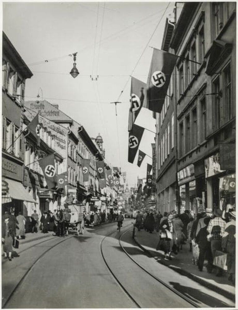 Foto der Hauptstrasse in Heidelberg in dene 40er Jahren des 20. Jahrhunderts. Die Häuser sind mit Hakenkreuzfahnen geschmückt.